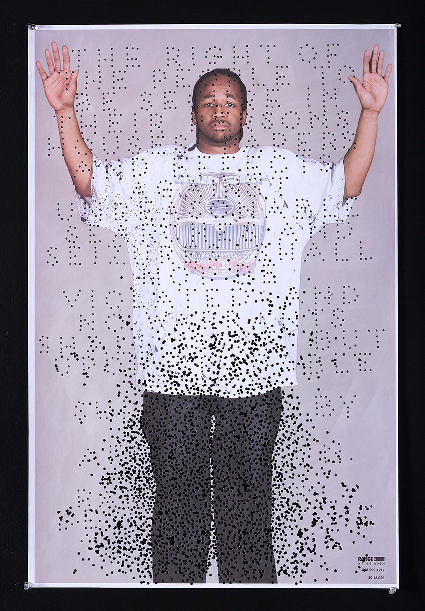 photo of a man with hands in air printed on a commercial shooting range with holes spelling out the IV amendment to the US Constitution