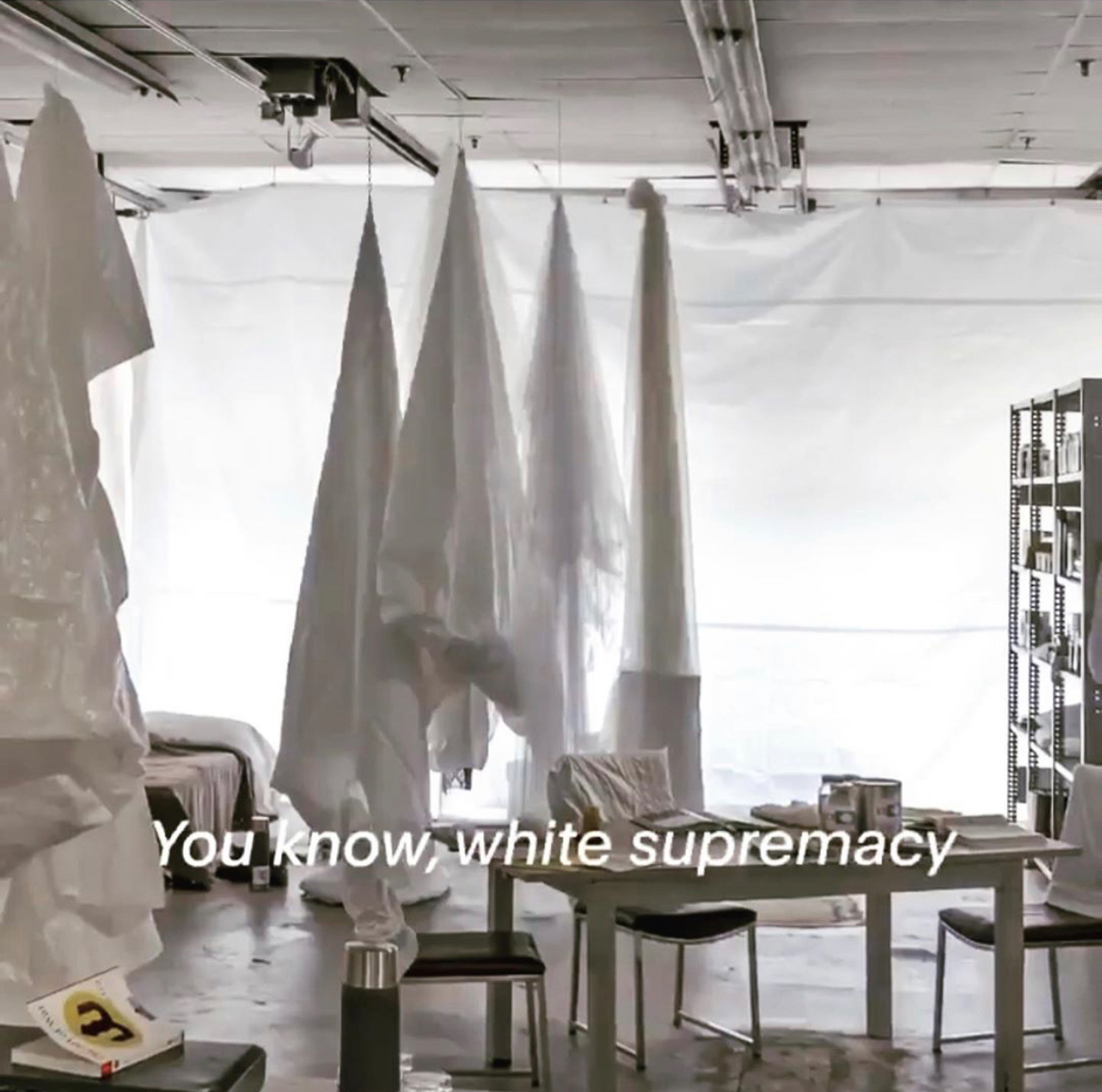 Antarctica art installation: sparse room wtih a table, chairs, bookshelf, hanging white shrouds and text "You know, white supremacy"