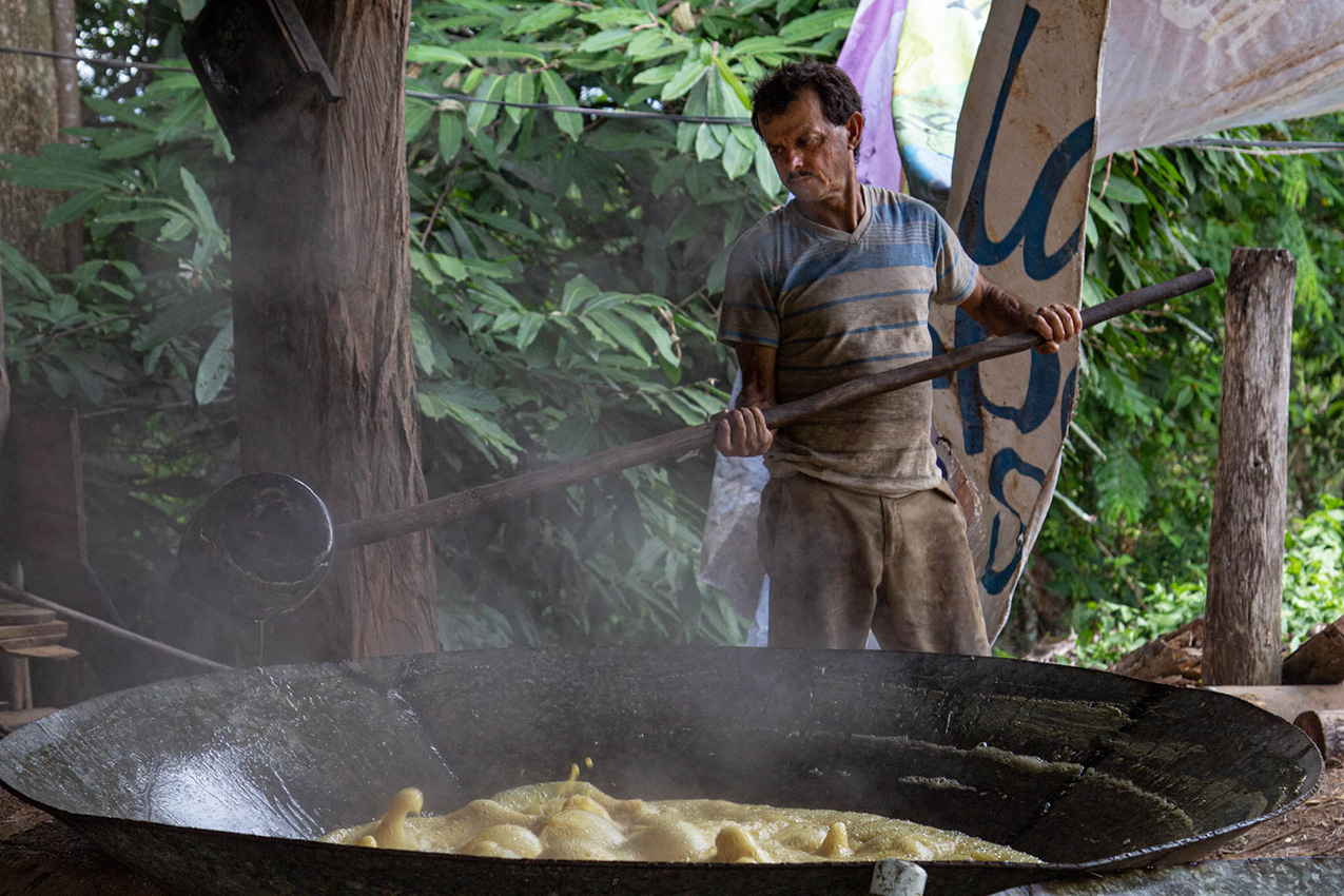 A Costa Rican man holding a large paddle stands next to a huge pan of steaming sugarcane