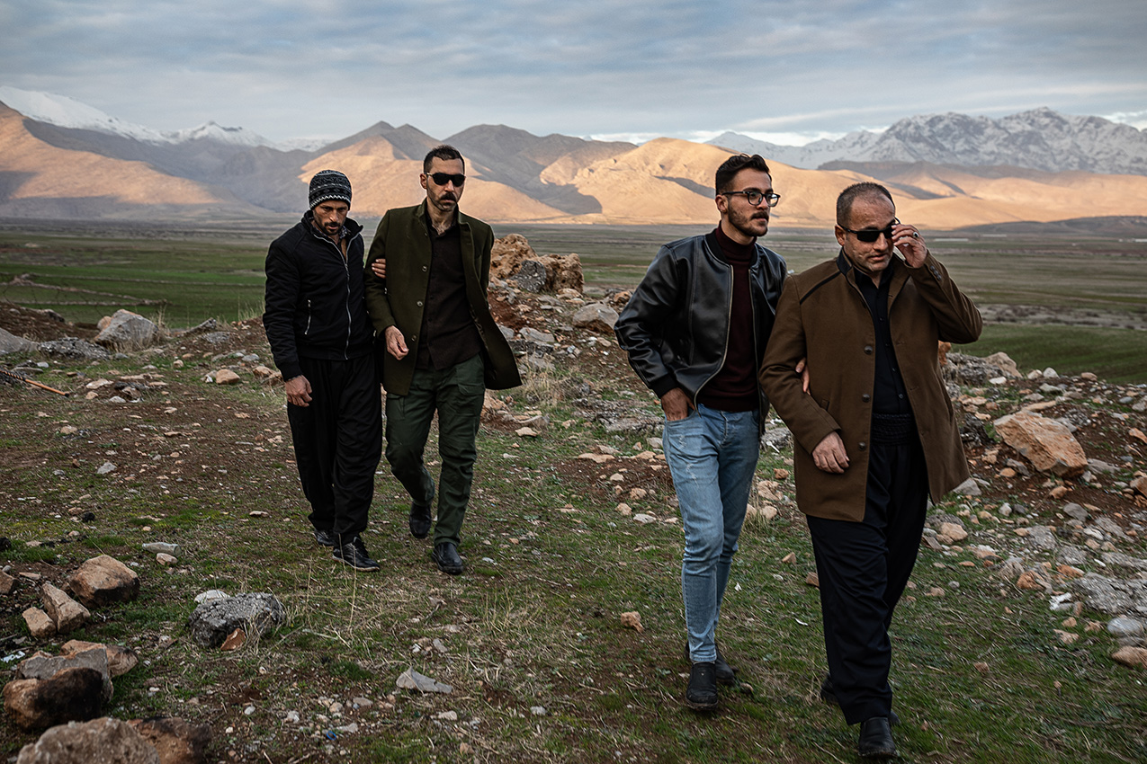 Two blind men wearing sunglasses are each accompanied by another man through a rocky landscape in Iraqi Kurdistan