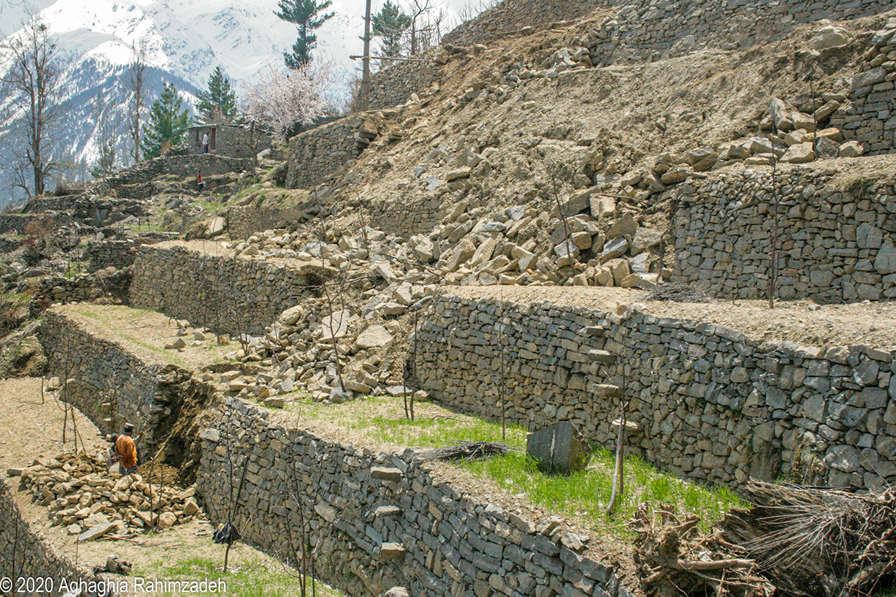 A man stands at the base of a terraced orchard in the Himalayas after a landslide has destroyed much of the stone terracing