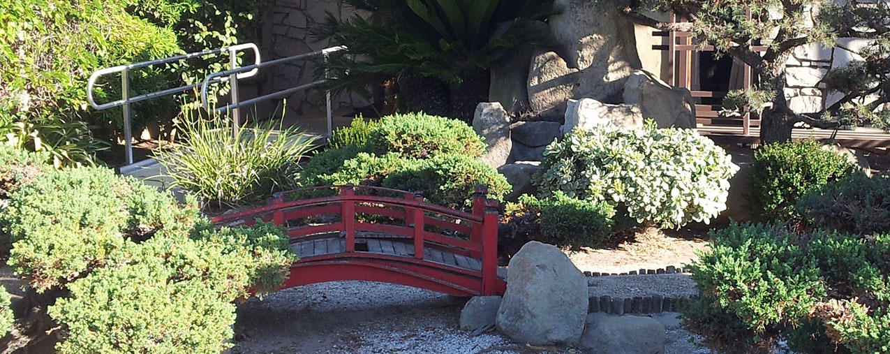 a karesansui niwa (dry garden) featuring a small red moon bridge over a gravel stream