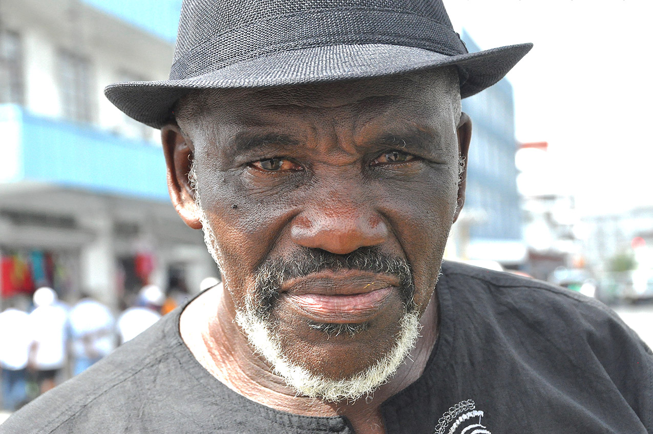 Close-up portrait of a dark-skinned man with a goatee and a dark hat on a street in Georgetown, Guyana