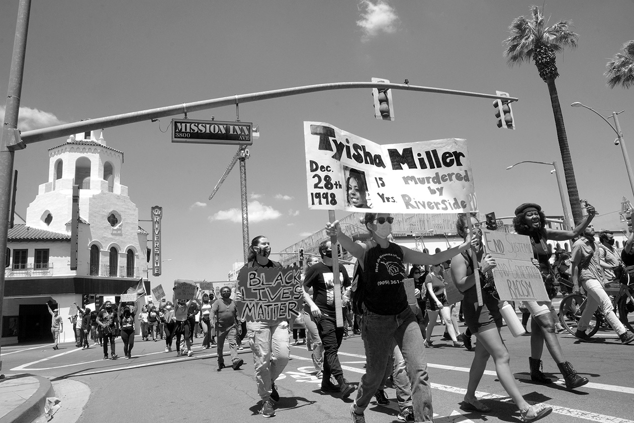 black and white photo of protesters marching in Riverside California, the front sign says "Tyisha Miller murdered by Riverside PD"