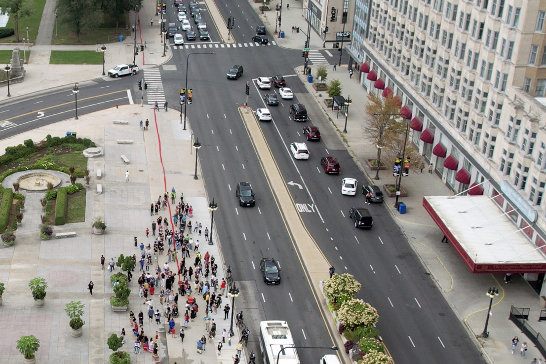 An overhead view of participants of the public art performance “Whose Lakefront” in downtown Chicago gathering around a line of red sand being poured to bring attention to the land taken from the Pokagon Band of Potawatomi Indians