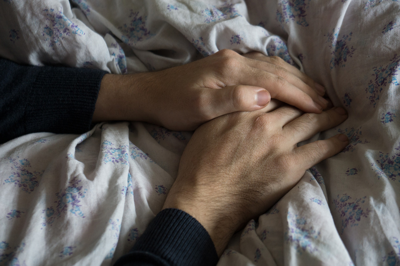 a young man's hands cupped over a floral bedspread