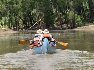 three or more people paddle a large canoe stuffed with their gear down the Mississippi River