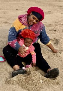 a black woman and her baby, both wearing red bonnets, play in the sand