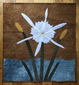a pictorial quilt featuring the bright white, showy blossom of a cahaba lily on a brown and blue backdrop