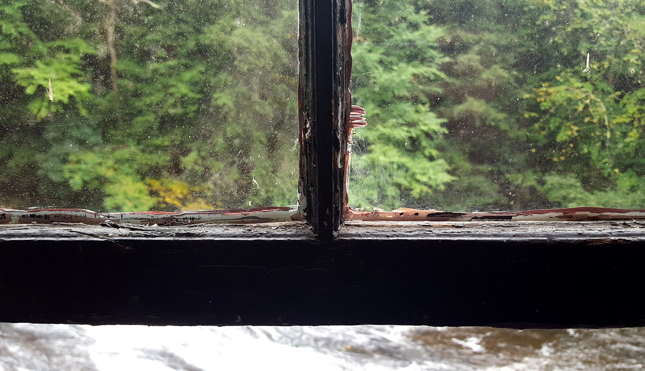 photo looking out a window that's divided into frames by the window pane. the top two glass panes show the green trees beyond, while the open area below the window frame reveals rushing water