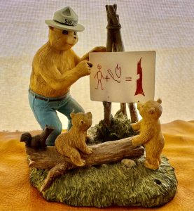 a figurine of Smokey the Bear teaching two bear cubs about fire using a drawing propped on an easel