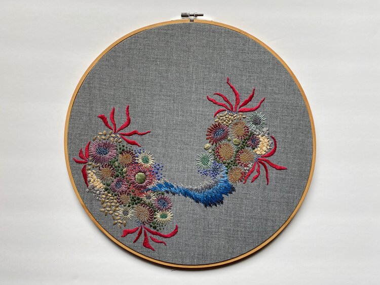 an embroidery hoop with gray fabric embroidered with an asymmetrical grouping of anemones and various coral in all colors