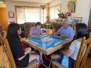 two young and two elderly people play mahjong on a green velvet table in a living room