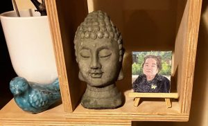 a small bookshelf niche with a buddha head sculpture and a miniature painting of the author's Popo (Grandma)