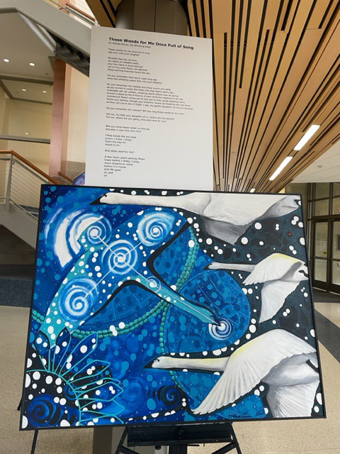 art installation of a blue, white and black painting of trumpeter swans meeting a swirling starry sky, below a printed poem
