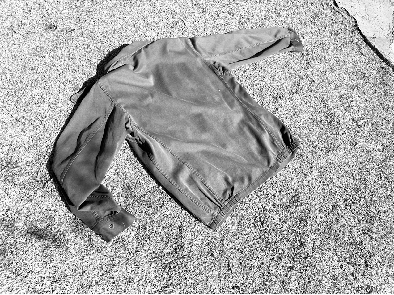 a black and white photo of a light-weight jacket laying on the grass with its back facing upwards