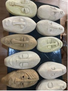 ten wooden masks in varying colors and styles, all with elongated faces