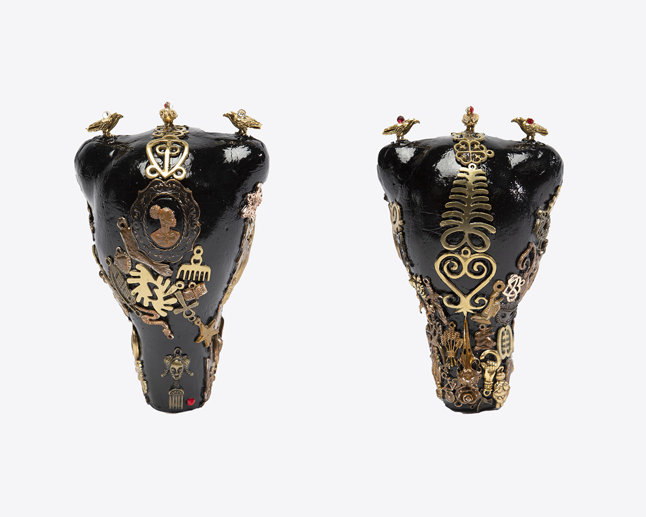 two womb-shaped black metal objects adorned with various copper and gold metal objects such as birds, a brooch, a hair pick, and various symbols