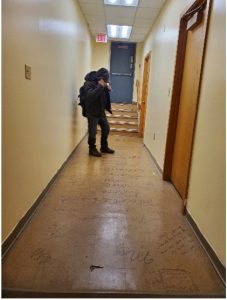 a person stands in an empty hallway; the tiled floor has writing on it