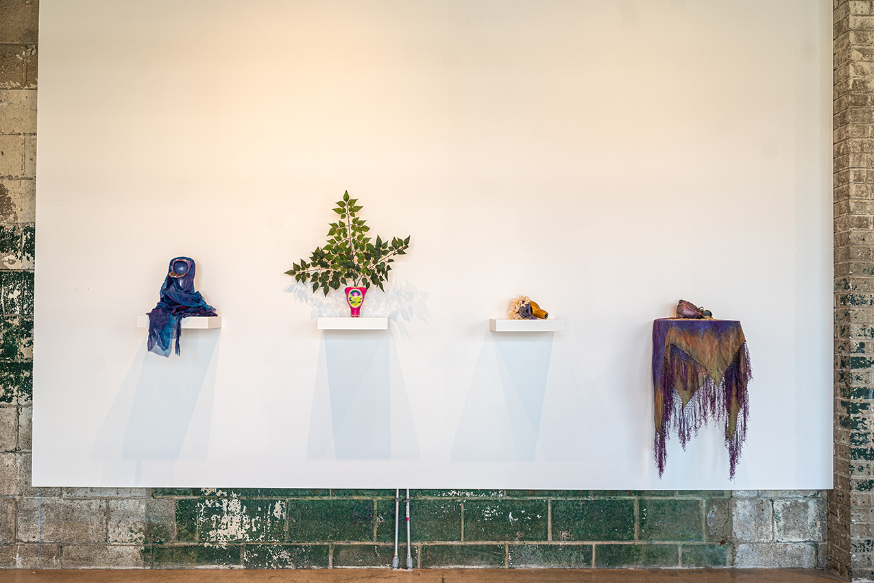 white wall with four simple white shelves, each holding a womb-shaped artifact with varied decorations
