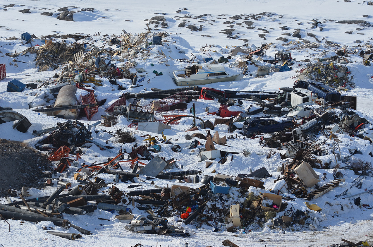 a landfill partially covered in snow; the scale is not immediately discernible but after a few moments a boat and a car can be identified, revealing the large scale of the pile of detritus.