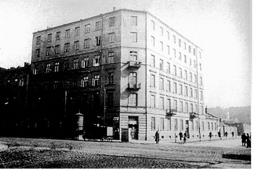 grainy historical photo of a 6-story building on the corner of a street. one side is blackened, though it is hard to tell if it is in shadow or blackened from fire
